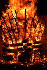 amazing violent bonfire of fire in a village in the dark night. The combustion of firewood creates big flames, flares, smoke, gas and generates a wide light around the square. Vertical photo.