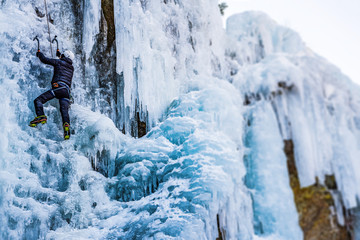 Ice Climbing Man with an Ice Axe and Crampons on a Frozen Waterfall