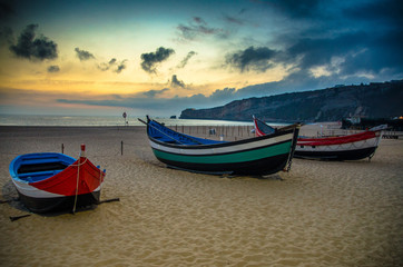 Fototapeta premium Portugal, Nazare beach, colored wooden boats, panoramic view of Nazare Town, Traditional Portuguese fishing boats in Nazare on the coast, blue clouds on the sky, white sand of beaches of Portugal