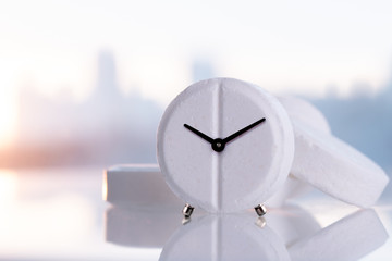 Alarm clock tablet on a white mirrored surface with copy space, close-up. Medicines with a clock on...