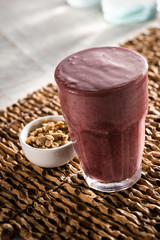 A glass of açaí juice or smoothie, with granola on a ramekin aside, with a table set background. Açaí is a very popular fruit in Brazil.