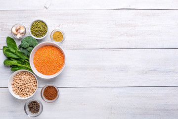 Spinach leaves and a bowl with chickpeas, lentils, mung and spices on a white wooden background. Background menu food.