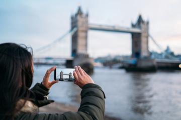 Woman taking a photo with the smart phone to the Tower Bridge in London on a sunny winter day,...