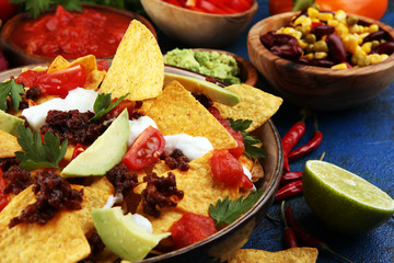 mexican nacho chips garnished with ground beef, guacamole, melted cheese, peppers and cilantro leaves in plate