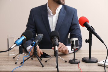 Businessman giving interview at table with microphones, closeup. Journalist conference