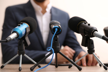 Businessman giving interview at table with microphones, closeup. Journalist conference
