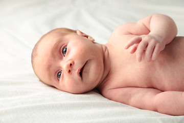 Baby girl lying on white bed, top view