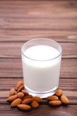 Almond milk in glass with almonds on brown wooden background