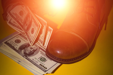 Concept photo of brown leather men's shoes, with dollars inside the shoes on a yellow background in the dark with lights