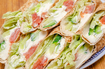 Tortilla rolls with salmon, tender cheese, lettuce and fresh cucumber close-up on a plate