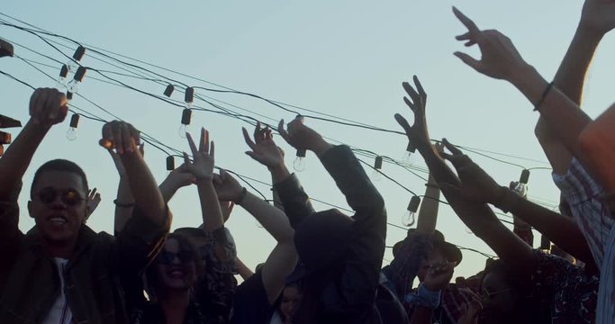 Hands of many young people rised up in the air while crowd dancing and jumping at the party or music festival on open air. Outdoor.
