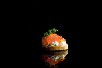 Caviar, red caviar on bread isolated on black background with reflections, copy space