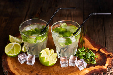 Fresh mojito in glasses with ice cubes on wooden table.