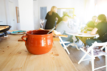 Casserole on the table and people sitting and eating food near window after culinary master class