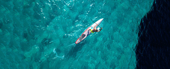 Obraz premium Aerial drone top down ultra wide photo of man practising in Stand Up Paddle or SUP board in tropical exotic sea