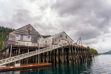 Old fish cannery in Ketchikan, Alaska. Abandoned factory of canned salmon. Tongass National Rain forest is on a background. Seasonal salmon fishing spot.