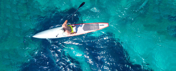 Obraz premium Aerial drone top down ultra wide photo of man practising in Stand Up Paddle or SUP board in tropical exotic sea