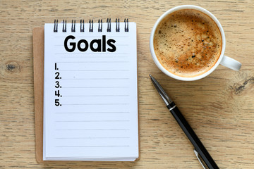 Goals text in the notebook on a wooden table. Top view - business concept.