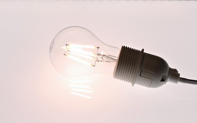 Hell leuchtende LED-Birne (ähnlich einer Glühbirne), in einer Fassung mit Stromkabel auf weißem, hellen Hintergrund; Symbolfoto für Idee und Erleuchtung