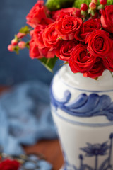 Coral Roses arranged in a Blue Vase with Blue Background on Wood Table