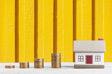 Stack golden coins with a mini house on desk