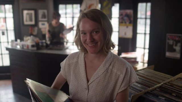 Portrait of a young woman holding a stack of vinyl records turns and smiles towards the camera