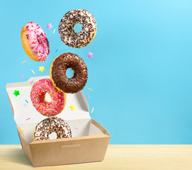 Donuts falling in paper box on blue background. Copy space