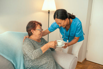 Supportive young nurse looking at elder woman. Smiling beautiful caregiver and disabled old lady at home. Friendly relationship between senior woman and caregiver