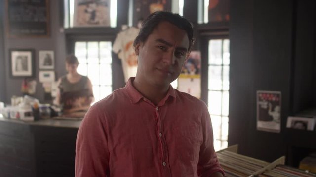 Portrait of a young hispanic man looking at a stack of vinyl records in a record store