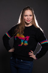 white Girl in a black sweater with rainbow stripes on a dark background. The girl’s hair is backlit.