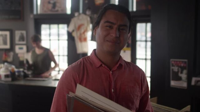 Portrait of a young hispanic man in a vinyl record store sturns and smiles at the camera