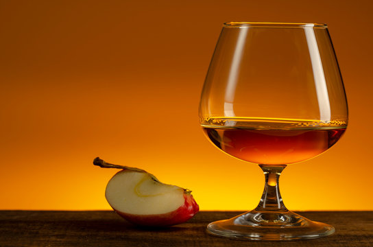 glass of Calvados Brandy and red apples on wooden table