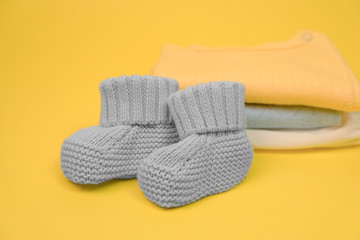 Little booties for newborn baby and heap on clothes on yellow background. Expecting a baby concept. Selective focus.
