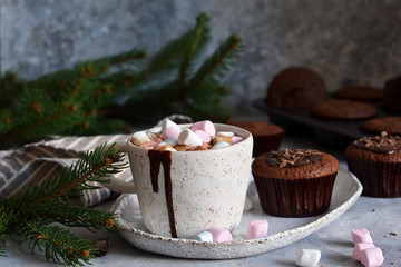 Christmas drink - hot chocolate with marshmallows and a cupcake on a concrete background.