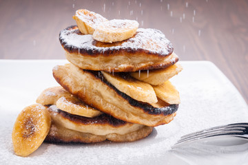 Pancakes with banana and powdered sugar falling on top