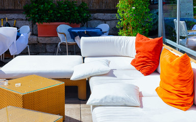Table and sofa at porch of cafe or restaurant at luxury resort on Sardinia Island in Italy in summer. Cozy veranda with chair and umbrella at Sardinian town in Sardegna. Mixed media.