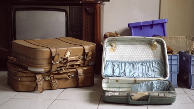 Close-up of old vintage travelling suitcases lying on the floor in abandoned room. A pile of used things and wooden furniture waiting for being moved to new apartment. Boxes full of stuff on the floor