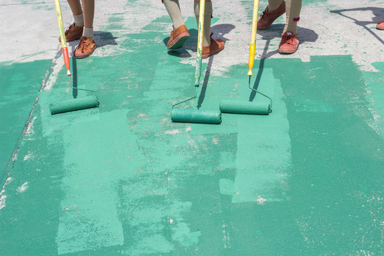 Hand painting a green floor with a paint roller for waterproofing