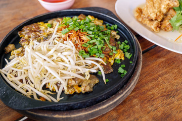 Chinese crispy Oyster omelette serve on hot iron pan on top with fresh bean sprout and chop scallion. 