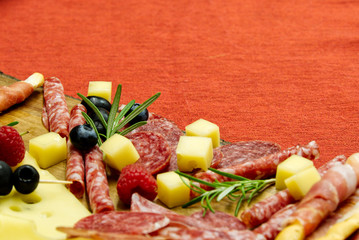 Meat and cheese plate antipasti snack with Prosciutto ham, Parmesan, Blue cheese, Cantaloupe melon and Olives on olive wood serving board on red background