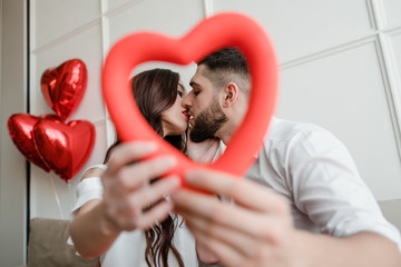 man and woman with heart shape in hands looking through at home with balloons