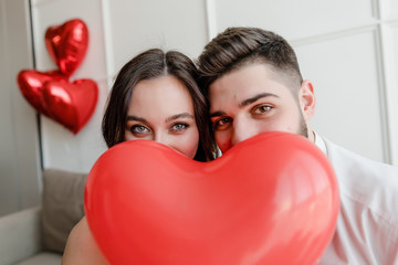 boyfriend and girlfriend with heart shaped balloon smiling and sitting on couch at home