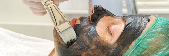 Beautician applies natural moisturizing mask to the face of a young beautiful woman. Black bamboo Charcoal Face Mask, applied to the face with a brush. panorama , banner
