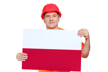 Portrait smiling middle-aged handsome worker wearing red hard hat, holding paper with polish flag in hands.