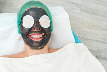 Young woman in a beauty salon with a black mask on her face. The concept of cosmetology. The...