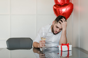 man at home drinking wine with present and heart shaped balloons at home