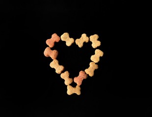 Dog croquettes forming a heart on black background. pets concept