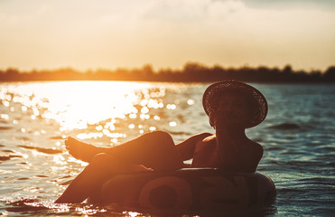 A man ware hat and he is on swim tube in the water.