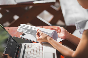 Fototapeta premium woman opening and reading a paper sheet near laptop on wooden table.