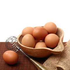 Wire whisk and brown eggs on white background